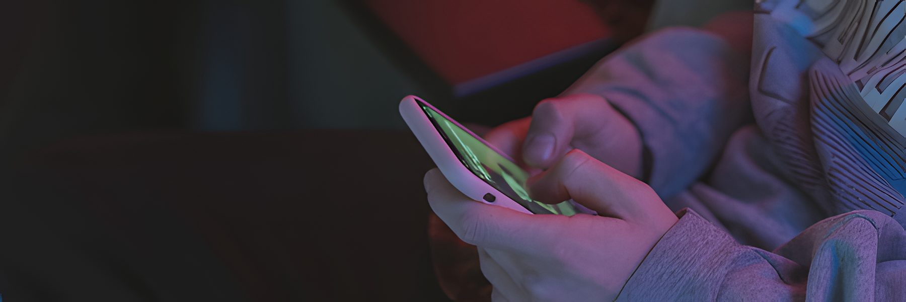 Hands holding a smartphone in neon light, viewing creator ads